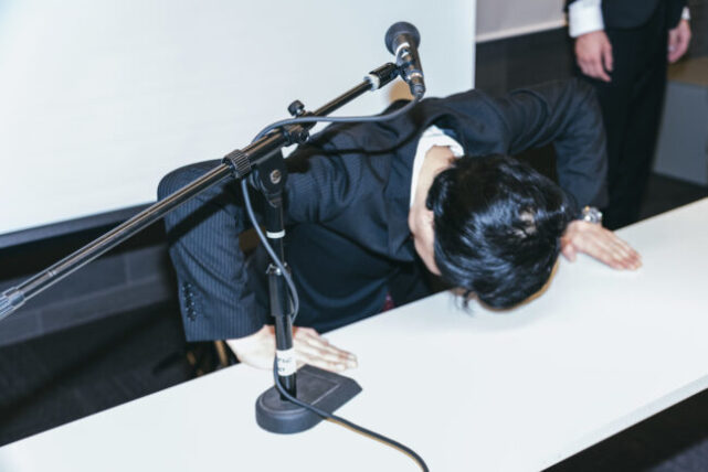テーブルの上で頭を下げる黒いスーツの男性